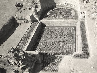 <p>Today, the walls of the diwan have been restored. When it was excavated, as shown in this photo, the room had to be cleared of the rubble of carved plaster that had fallen from the walls and ceiling. This photo also shows the diwan&rsquo;s inner, apsidial platform, with the Tree of Life motif, which appears in full in this calendar&nbsp;in December.</p>
