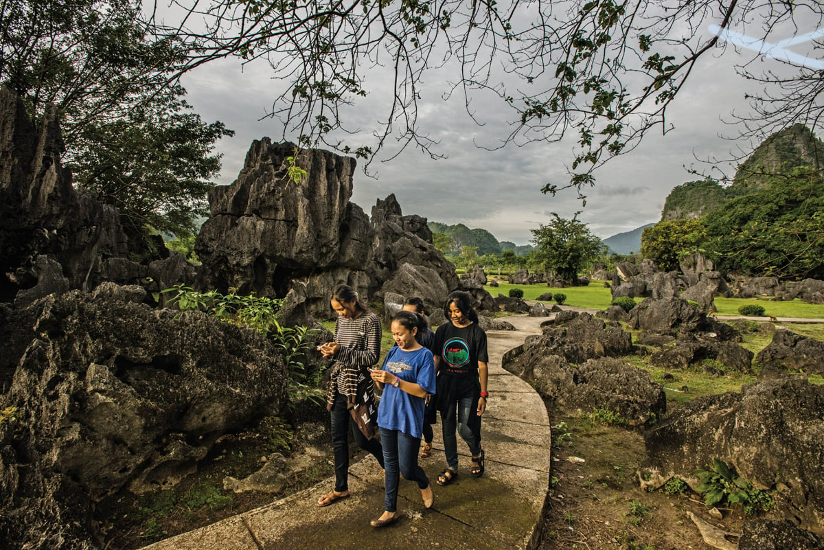 <p>Teenagers stroll along a path in Leang-Leang Prehistoric Park, where the cave art is well documented; however, most of the 127 known caves lie outside the park&rsquo;s boundaries, and so far, only 90 have been surveyed.</p>
