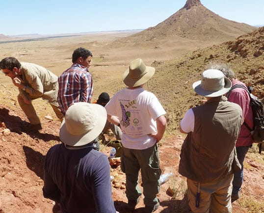 <p>Paleontologist Nizar Ibrahim, far left, leads a team exploring the Kem Kem escarpment on the once-swampy edge of the Sahara Desert in southeastern Morocco, a region Ibrahim dubs &ldquo;The River of Giants&rdquo; for its treasures of fossilized bones of large dinosaurs. Largest among them, and adapted to both water and land, was&nbsp;<em>Spinosaurus aegyptiacus.</em></p>
