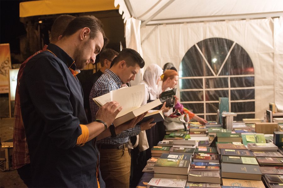 <p><em>Above</em>: Sarajevo remains a city of bibliophiles. Here, residents and visitors browse at a Ramadan book fair.&nbsp;<em>Below, right</em>: Tourist souvenirs brighten a window in a <em>bezistan </em>(bazaar) shop in the Baščaršija, Sarajevo’s commercial and cultural center.</p>
