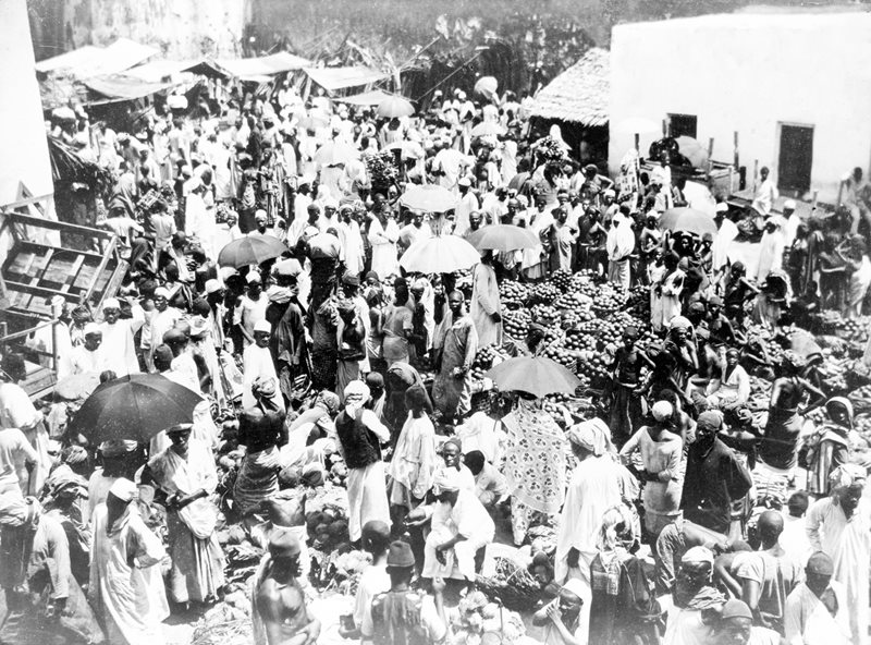 An early 20th-century photograph shows a market in Stone Town, a center for trade throughout the East African coast and Indian Ocean region since the 12th century, under Portugal, Oman, Britain and Tanzania. The Portuguese imported a printed Indian calico they called <em>leso</em>, which by the 19th century developed into the two-piece, block-printed cotton wrap that was named kanga in Swahili&mdash;a reference to the plumage of an eponymous guinea fowl.
