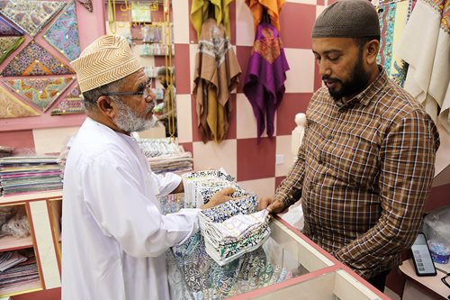 A street vendor, having unloaded hundreds of kummahs, finalizes a sell in the backstreets of Muscat, where each kummah’s unique design becomes a personal statement. 